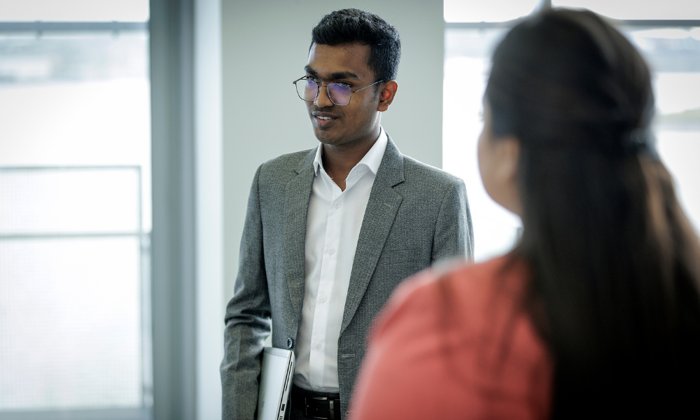 A student in a professional outfit holds a laptop in a workplace