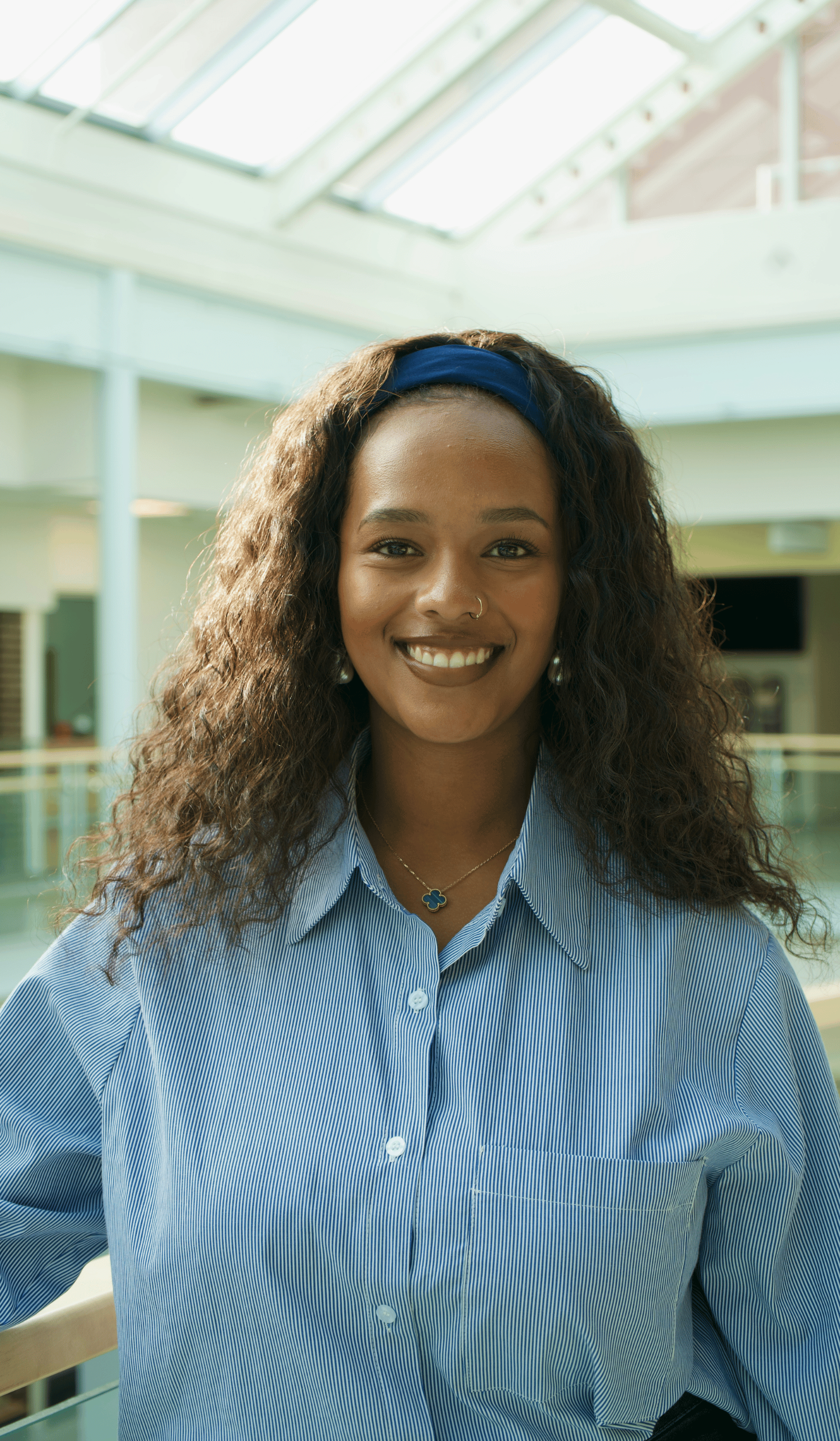 Dinah is a Black woman with long curly brown hair. She wears a blue and white shirt and headband