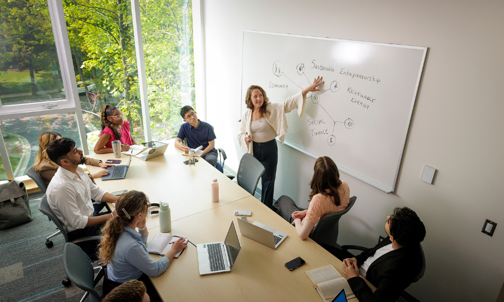 A professor points to information on a white board to a small class