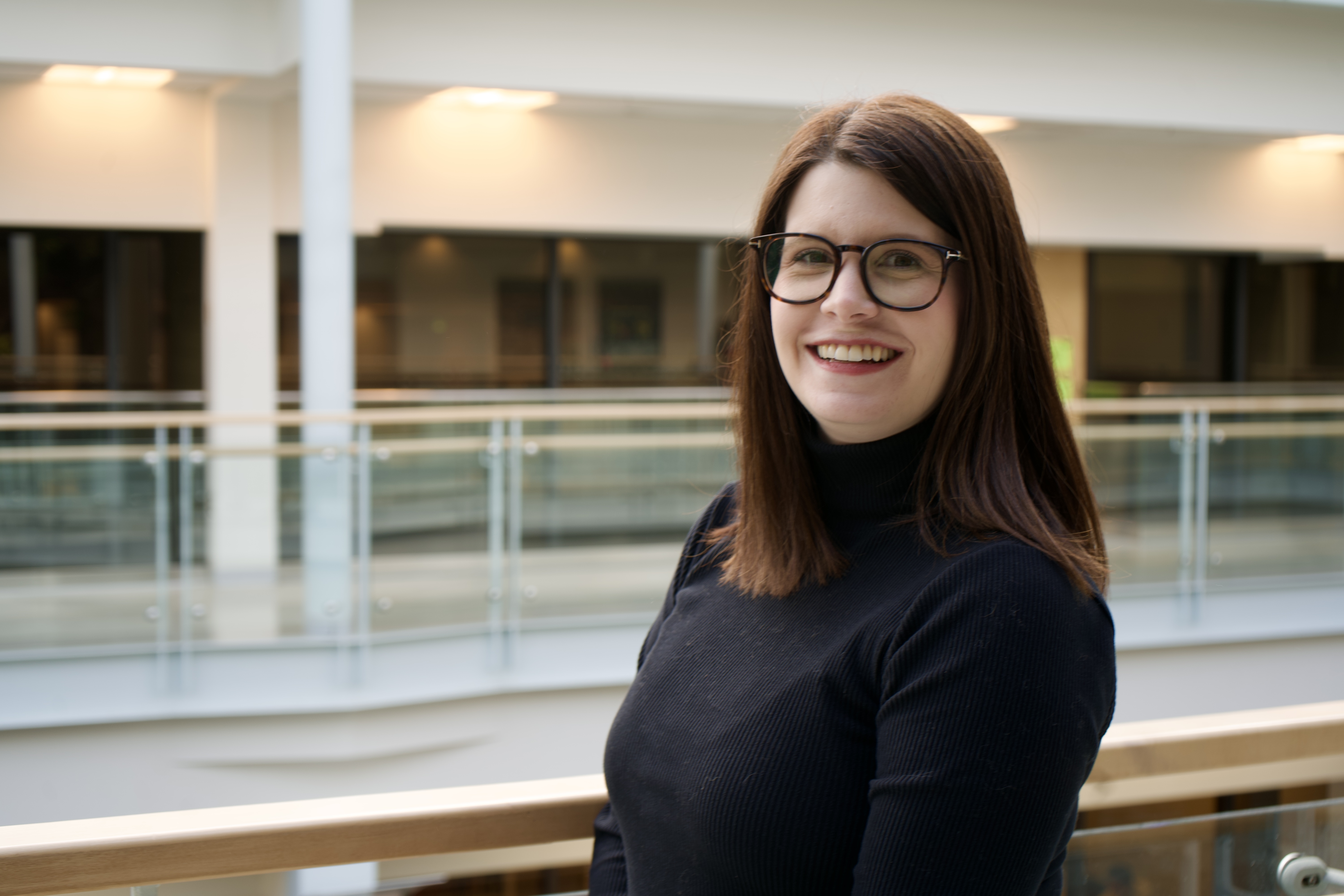 Kristen is a white woman with brown hair. She wears black glasses and a black turtleneck sweater