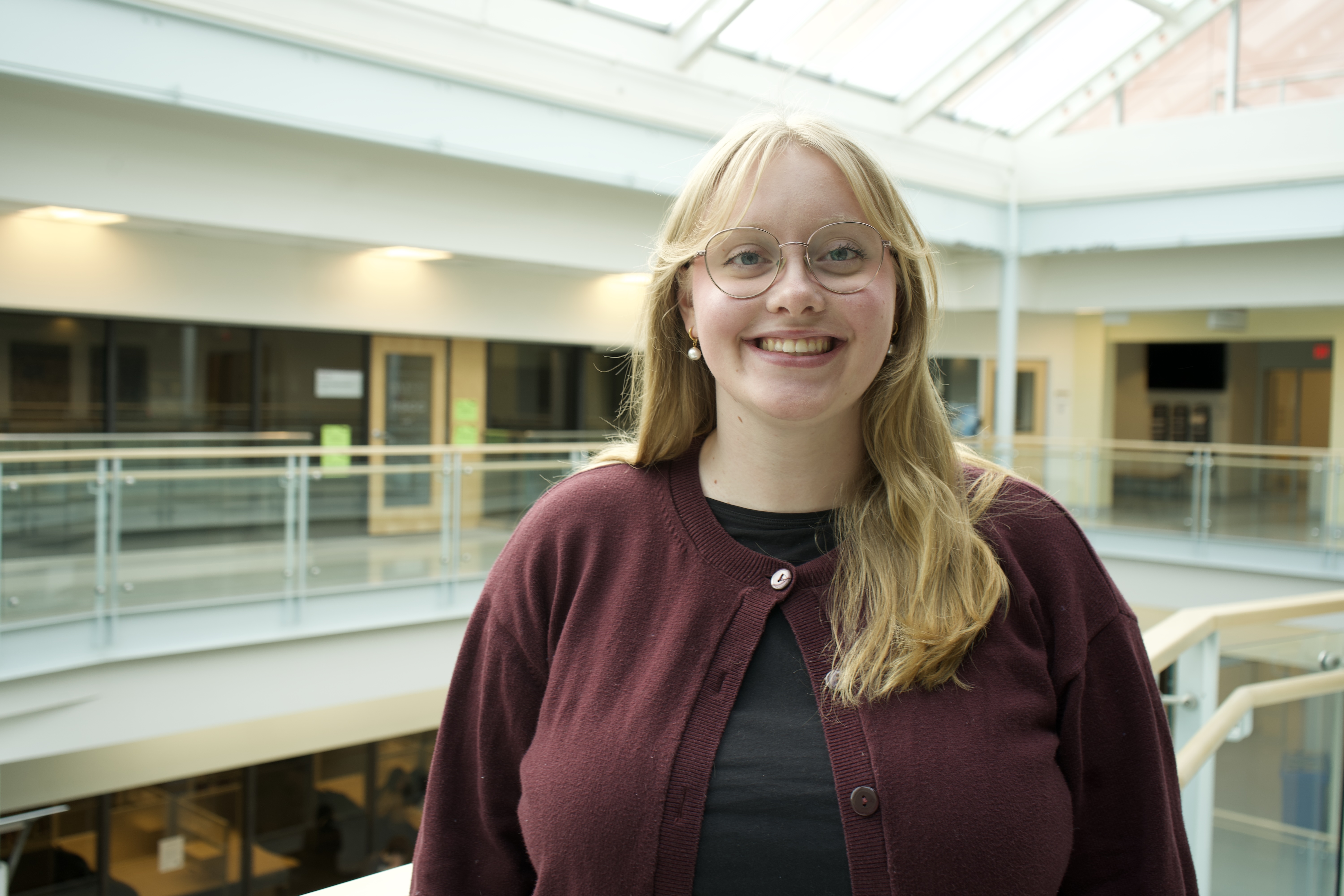Maggie with a white woman with long blonde hair. She wears a maroon cardigan and has glasses.