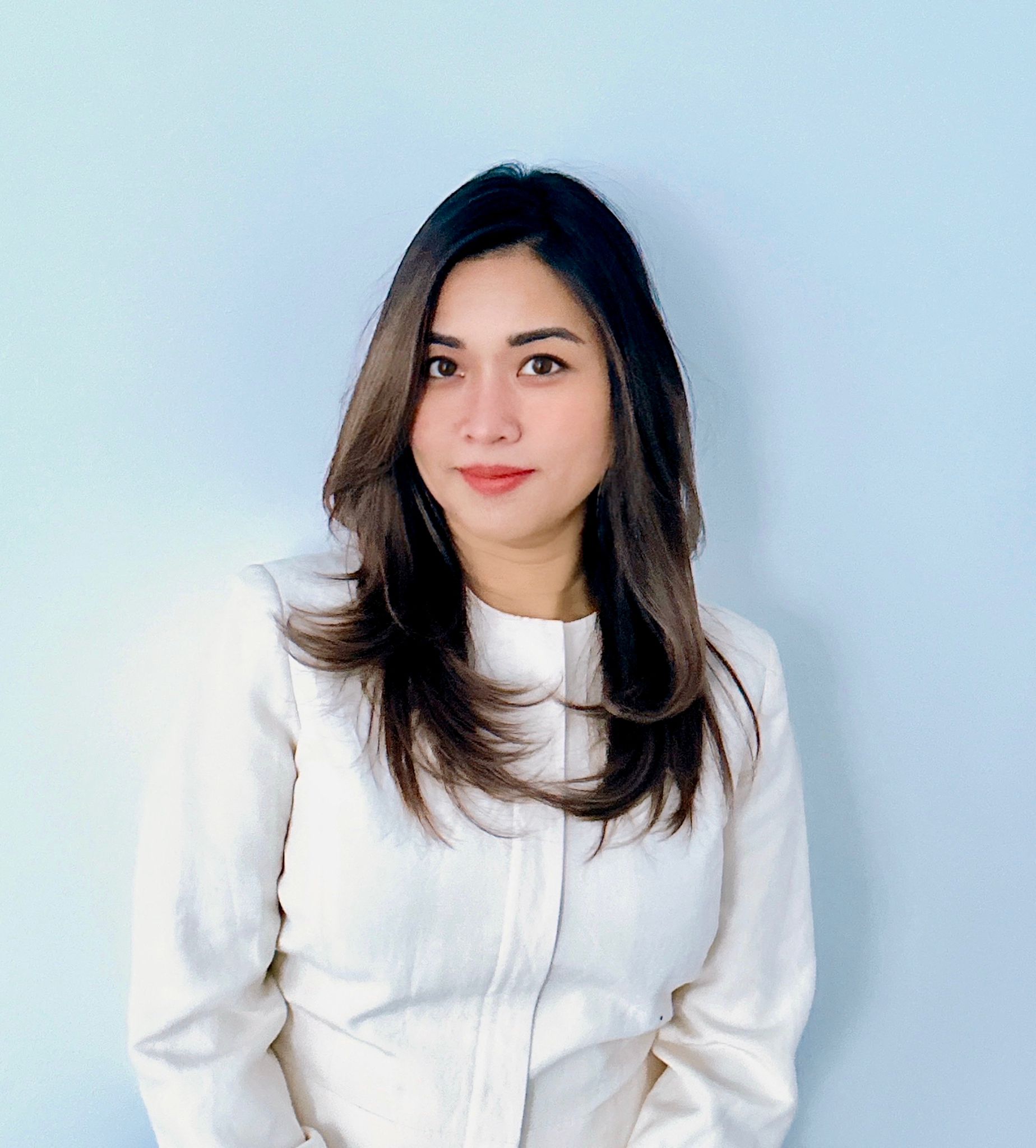 May is a woman with long brown hair with highlights. She wears a white shirt.