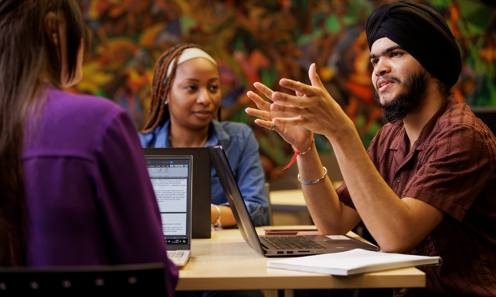 Three students talk together inside the library