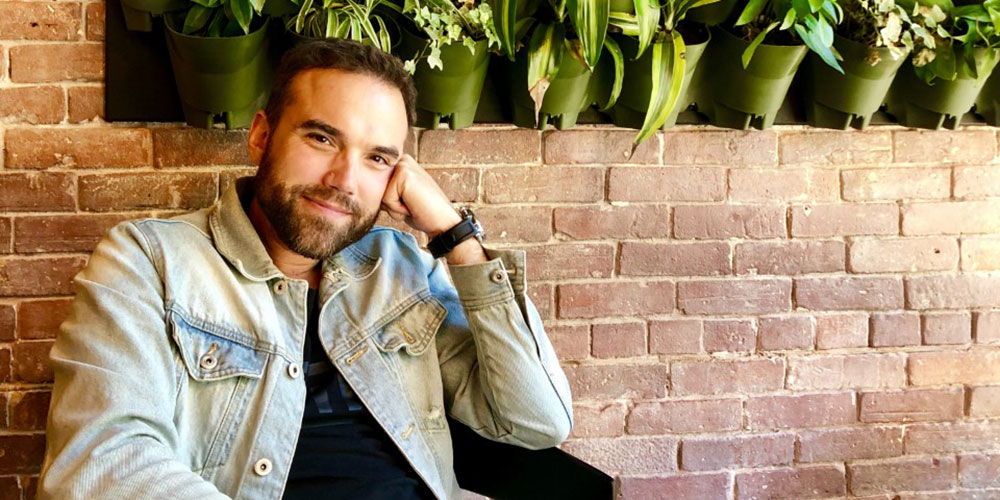 Ian MacLeod sitting in front of a brick wall and potted plants.