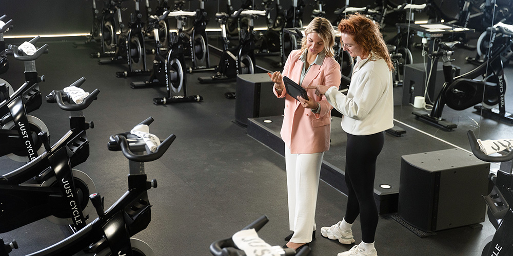 Two people consult over a computer in a gym filled with stationary bicycles.