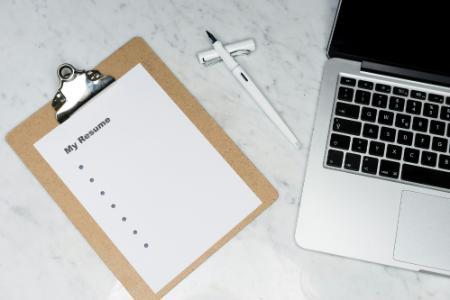 Photo of a laptop and a clipboard with a resume on it