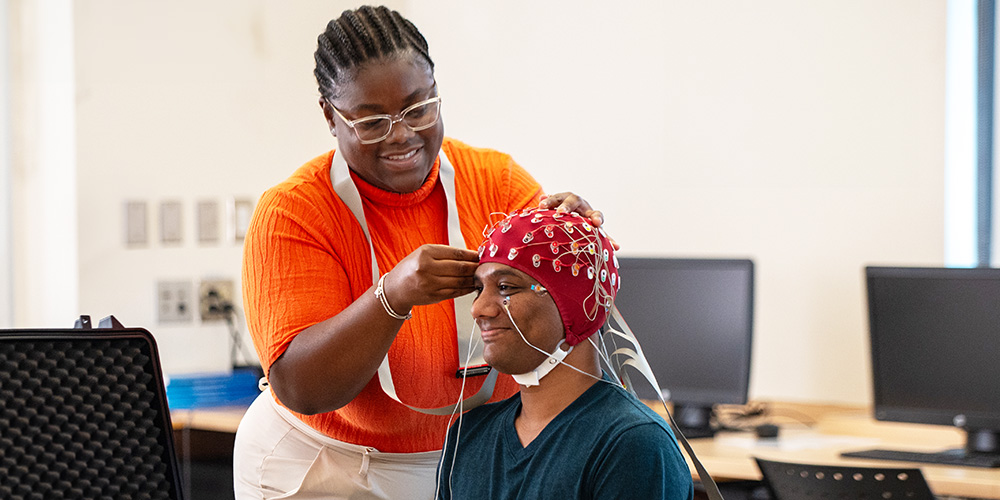 A student attaches sensors to the head of a person.