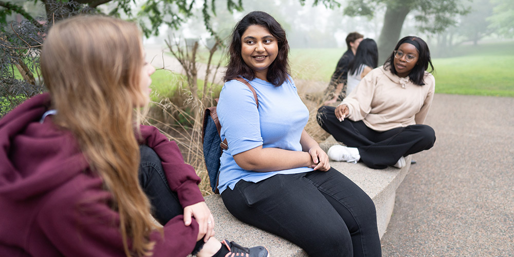 Three students sitting on a bench, chatting.